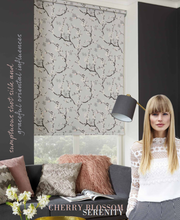 Load image into Gallery viewer, A woman standing in a room with roller blinds featuring a floral pattern. The room has a sofa, armchairs, and a lamp with a beige shade.